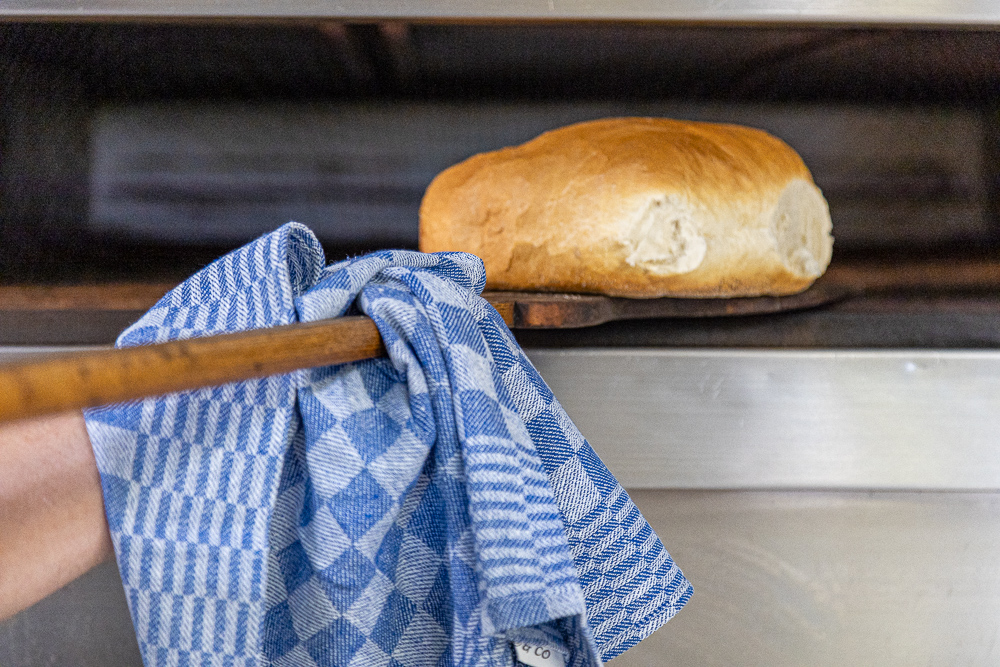 Visual van een brood in de oven en een keukenhanddoek op de voorgrond.